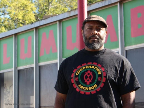 Kali Akuno of Cooperation Jackson standing in front of mural